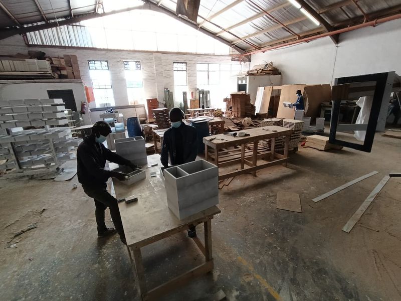 Spacious industrial workshop featuring high ceilings with exposed steel trusses, concrete flooring, and large windows providing ample natural light for manufacturing operations.