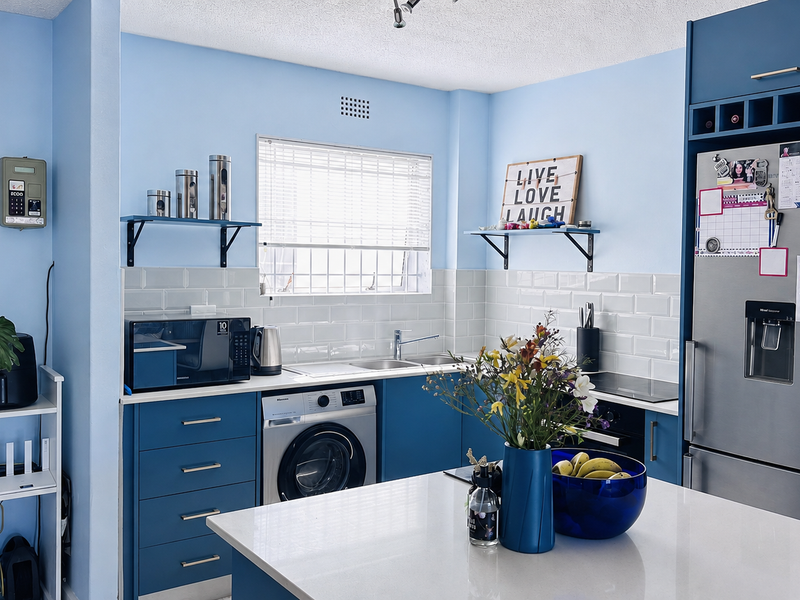 A functional kitchen featuring blue cabinetry, white subway tile backsplash, quartz countertops, and integrated appliances including a washing machine and oven.