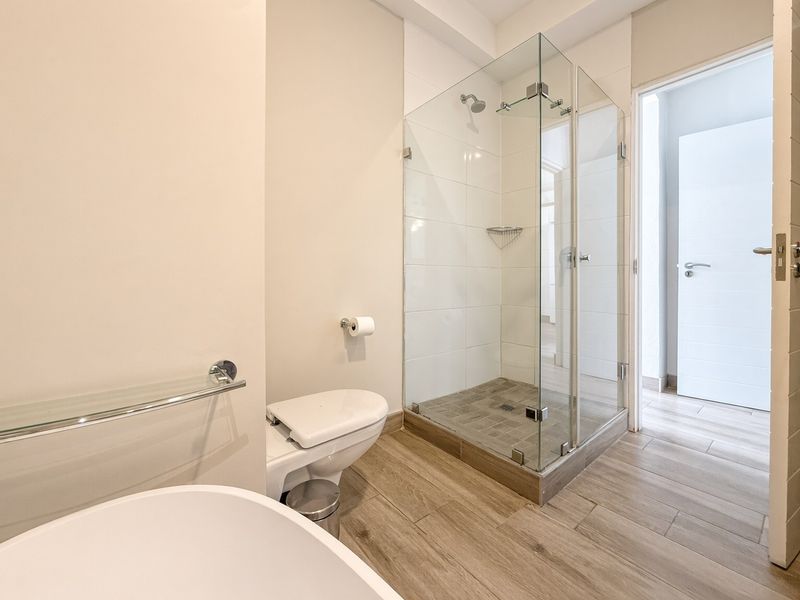 Modern bathroom featuring a glass-enclosed shower, wall-mounted toilet, and contemporary wood-look tile flooring, presenting a clean and well-maintained aesthetic.