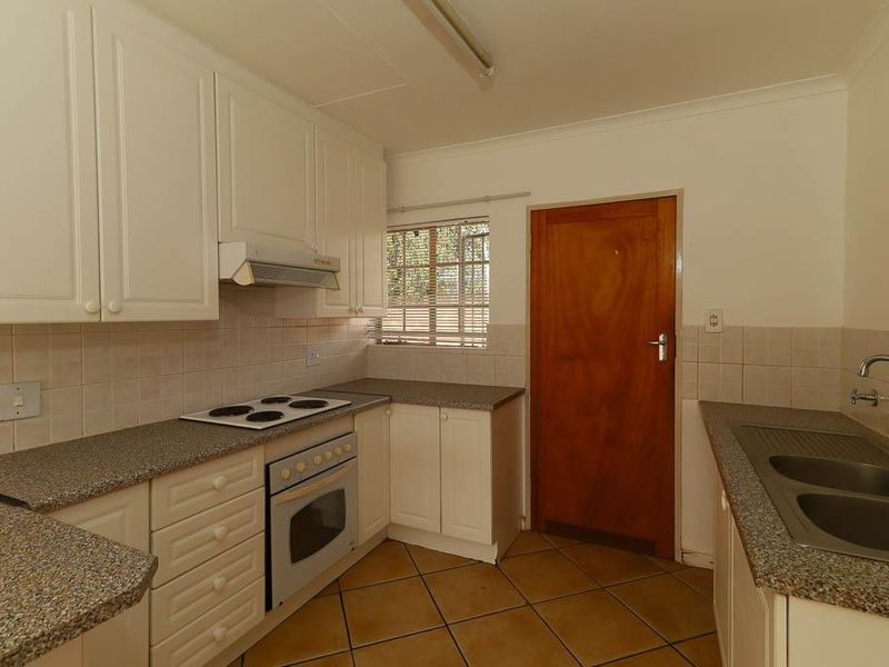 A functional kitchen featuring white cabinetry, laminate countertops, an electric hob, built-in oven, and tiled flooring, offering a clean and practical workspace.