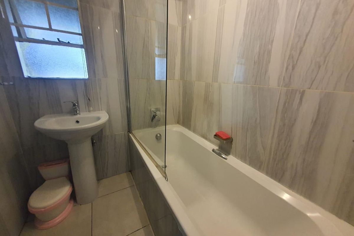 A modern bathroom featuring floor-to-ceiling marble-look wall tiles, a pedestal basin, and a bathtub with a glass shower screen.
