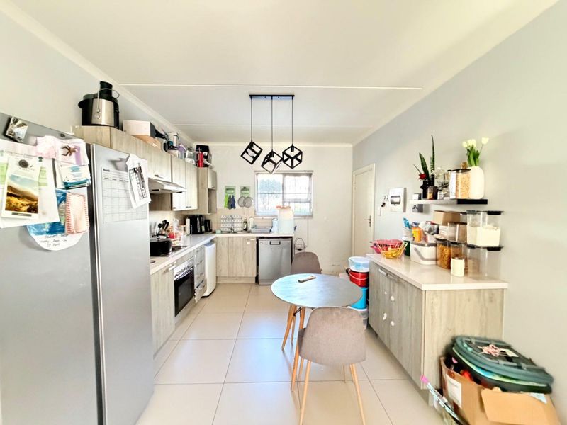 A functional kitchen featuring light wood-finish cabinetry, tiled flooring, integrated appliances, and a dedicated dining area with modern pendant lighting.