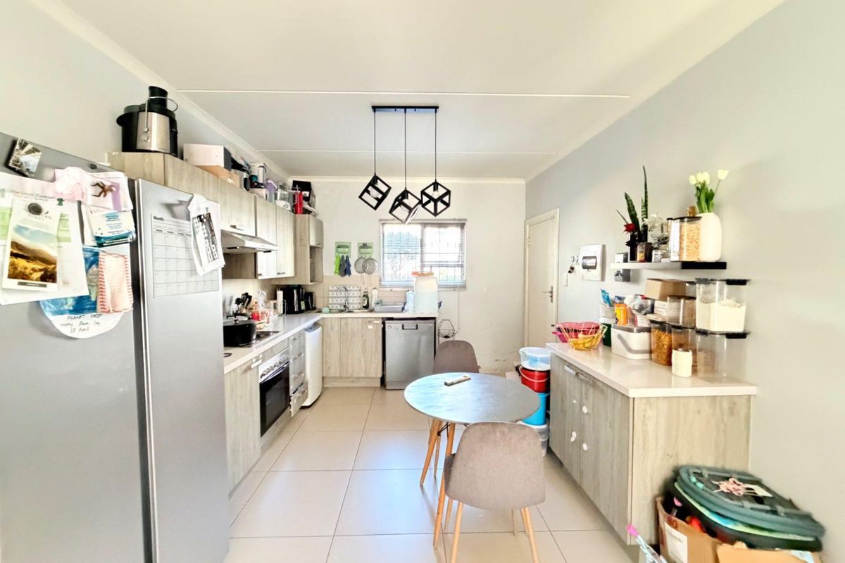 A functional kitchen featuring light wood-finish cabinetry, tiled flooring, integrated appliances, and a dedicated dining area with modern pendant lighting.