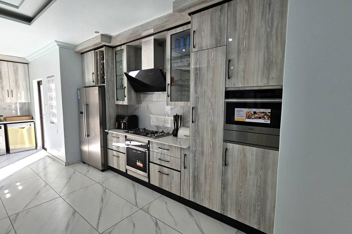 Modern kitchen featuring wood-grain cabinetry, marble-look floor tiles, built-in oven, gas hob, extractor fan, and integrated laundry appliances.