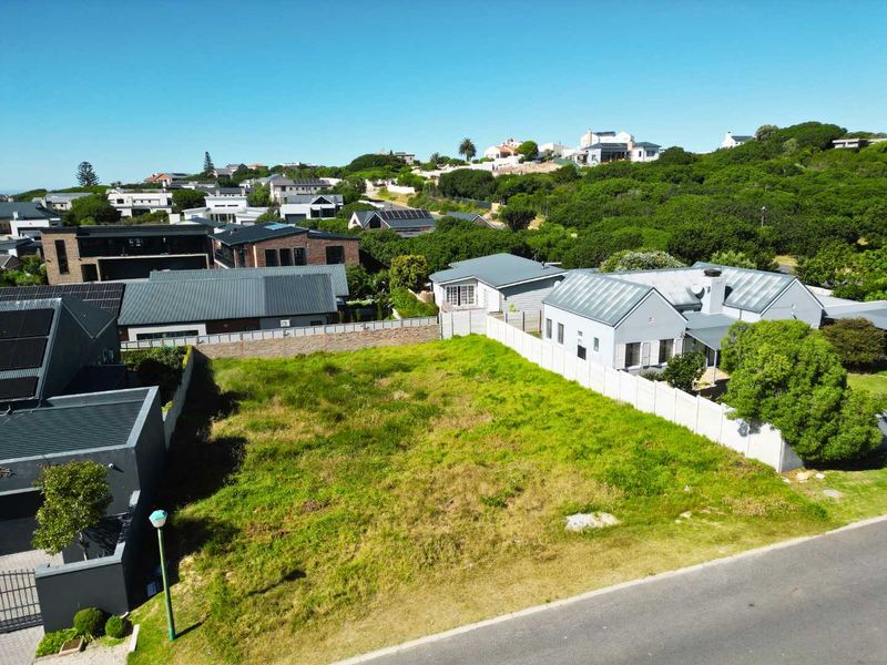 Aerial view of a vacant residential plot situated in a developed neighborhood, featuring established boundary walls and street access.