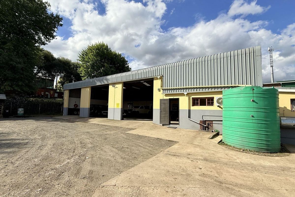Industrial warehouse facility featuring large open bays, corrugated metal roofing, and an external water storage tank on a spacious gravel yard.