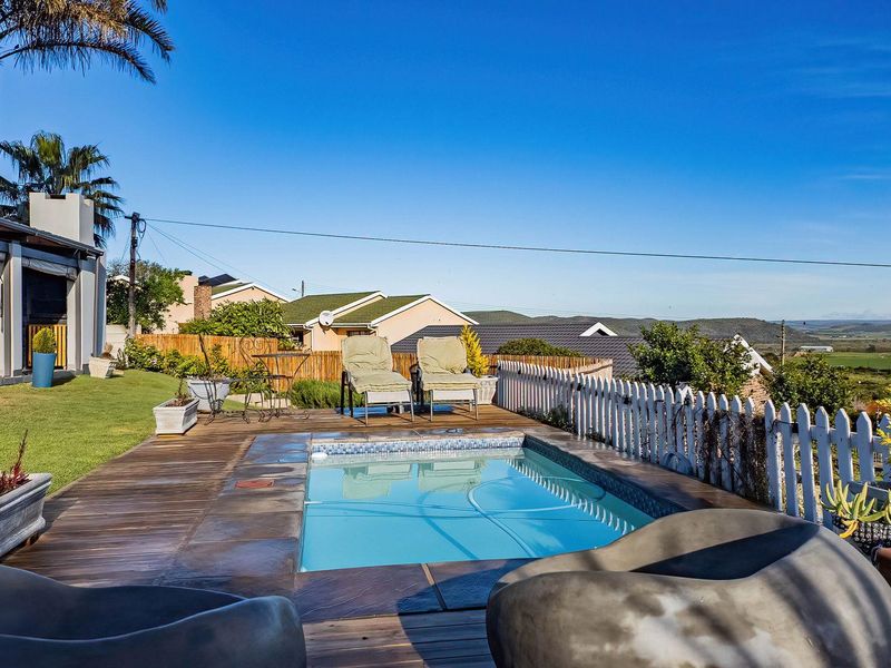 Outdoor pool area featuring timber decking, a picket fence, and a covered patio, offering scenic views of the surrounding landscape.