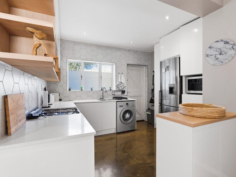 Modern kitchen featuring white cabinetry, quartz countertops, hexagon tile backsplash, polished concrete floors, and integrated appliances including a gas hob and microwave.