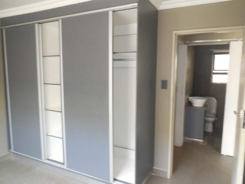 A clean bedroom featuring a modern built-in sliding door wardrobe with integrated shelving and an adjacent doorway leading to an en-suite bathroom.