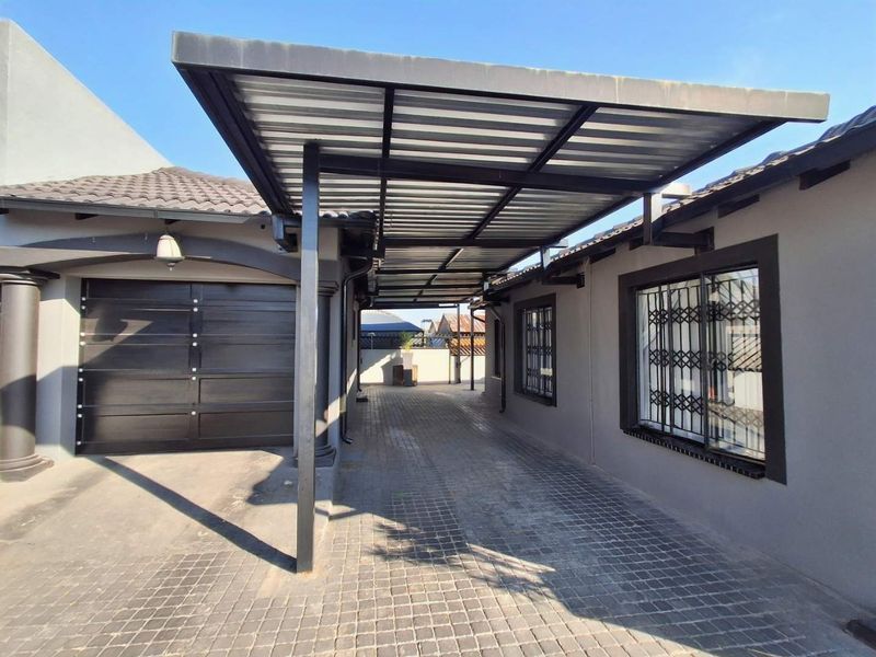 A well-maintained paved driveway featuring a modern metal carport structure, providing covered parking adjacent to the garage and main building entrance.