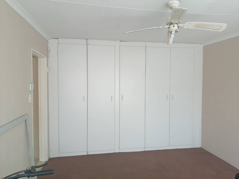 A bedroom featuring extensive built-in cupboard storage, a ceiling fan, and neutral wall finishes, offering a blank canvas for renovation.