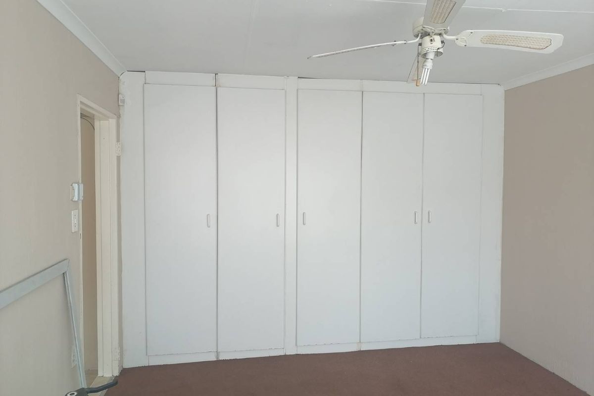 A bedroom featuring extensive built-in cupboard storage, a ceiling fan, and neutral wall finishes, offering a blank canvas for renovation.