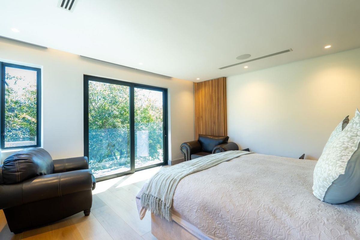 Modern bedroom featuring light timber flooring, recessed ceiling lighting, integrated air conditioning vents, and floor-to-ceiling sliding glass doors opening to a balcony.