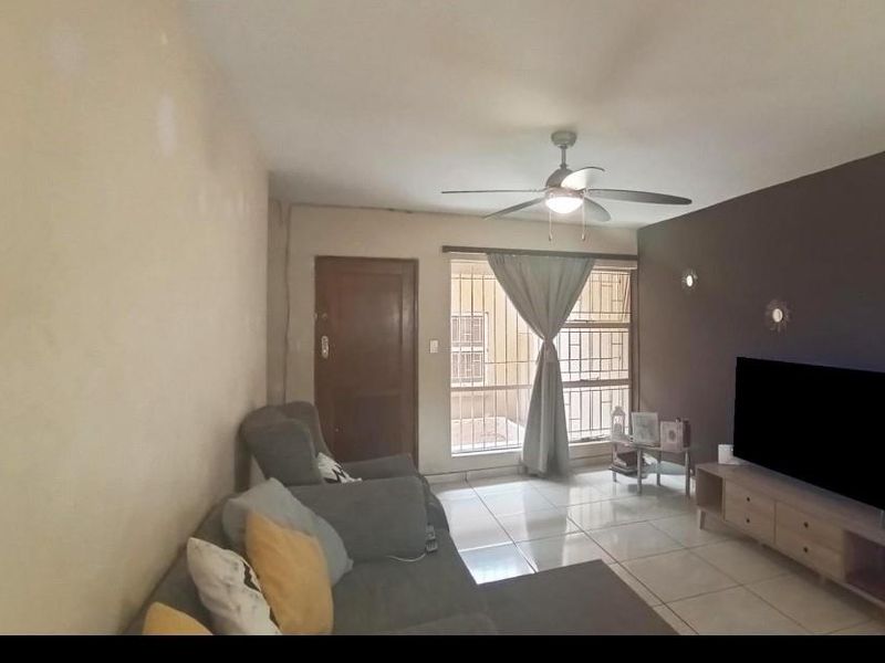 A living room featuring tiled flooring, a ceiling fan, and a sliding door with security bars, providing access to the exterior.