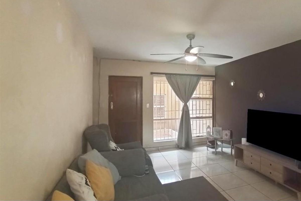 A living room featuring tiled flooring, a ceiling fan, and a sliding door with security bars, providing access to the exterior.