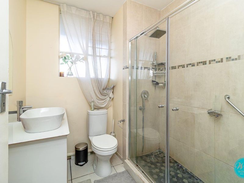 A functional bathroom featuring a vessel sink vanity, a toilet, and a glass-enclosed shower with both rain and handheld shower heads.