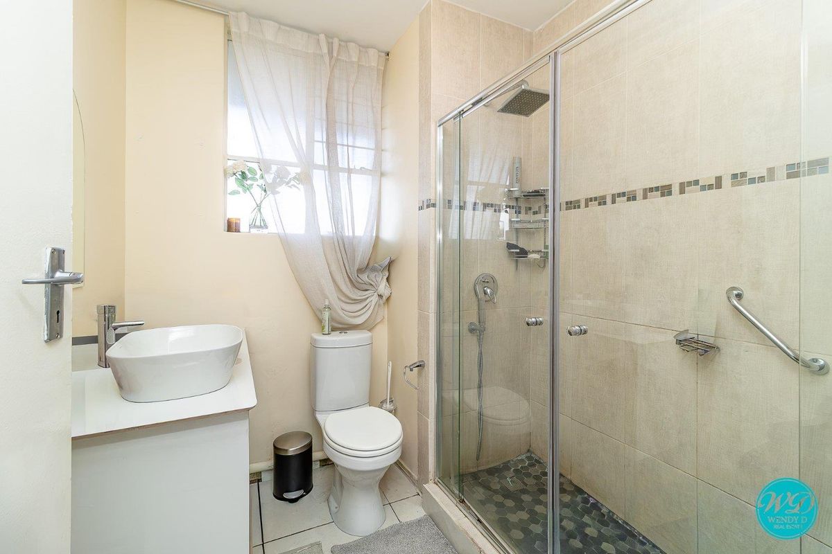 A functional bathroom featuring a vessel sink vanity, a toilet, and a glass-enclosed shower with both rain and handheld shower heads.