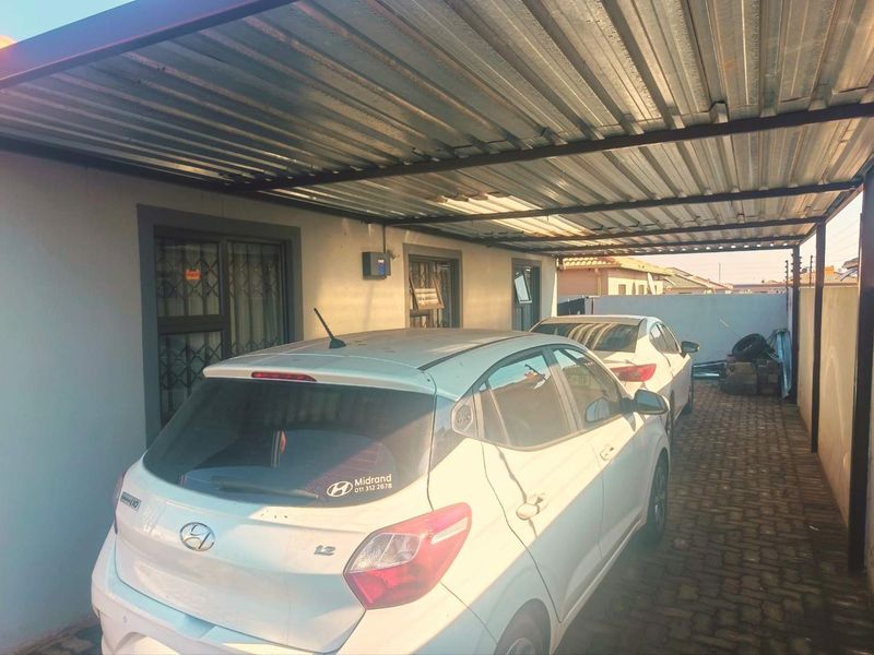 A covered carport area featuring a corrugated metal roof and paved flooring, providing sheltered parking space alongside the property.