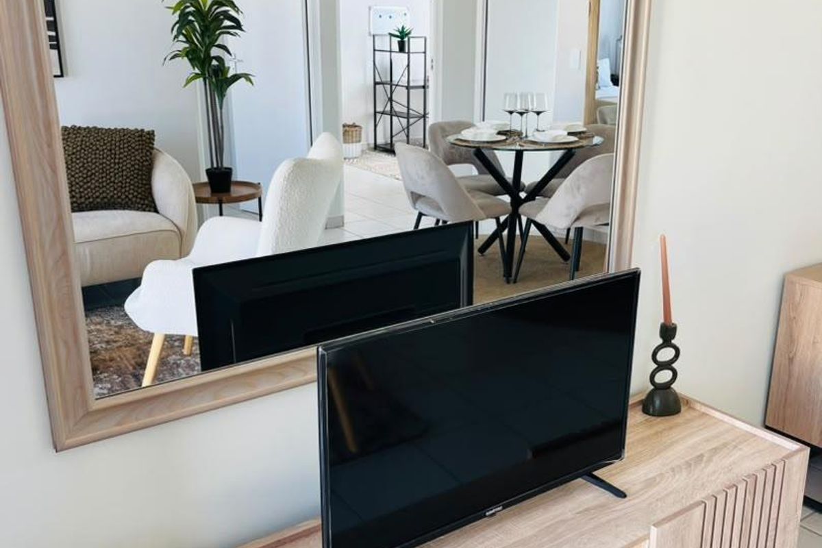 A bright living area featuring neutral tiled flooring and a large decorative wall-mounted mirror reflecting the adjacent dining space.