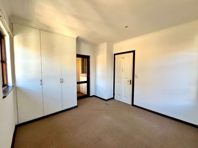 A bright, empty bedroom featuring neutral walls, carpeted flooring, and built-in cupboards, offering a clean canvas for personalization.
