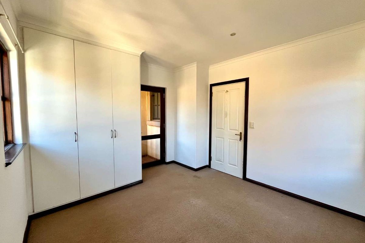 A bright, empty bedroom featuring neutral walls, carpeted flooring, and built-in cupboards, offering a clean canvas for personalization.