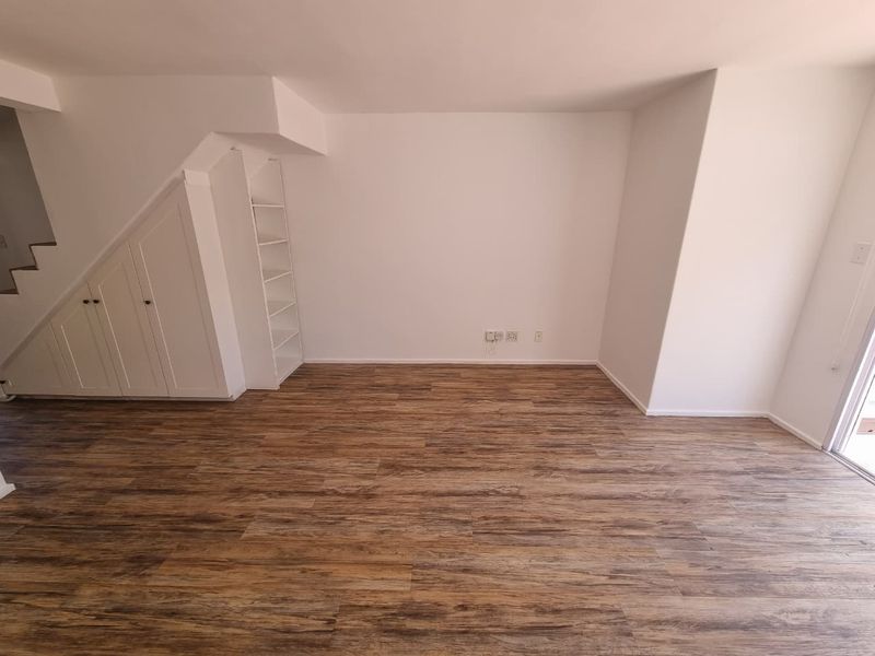 An empty living room featuring wood-look laminate flooring and convenient built-in under-stair storage cabinetry with integrated shelving.
