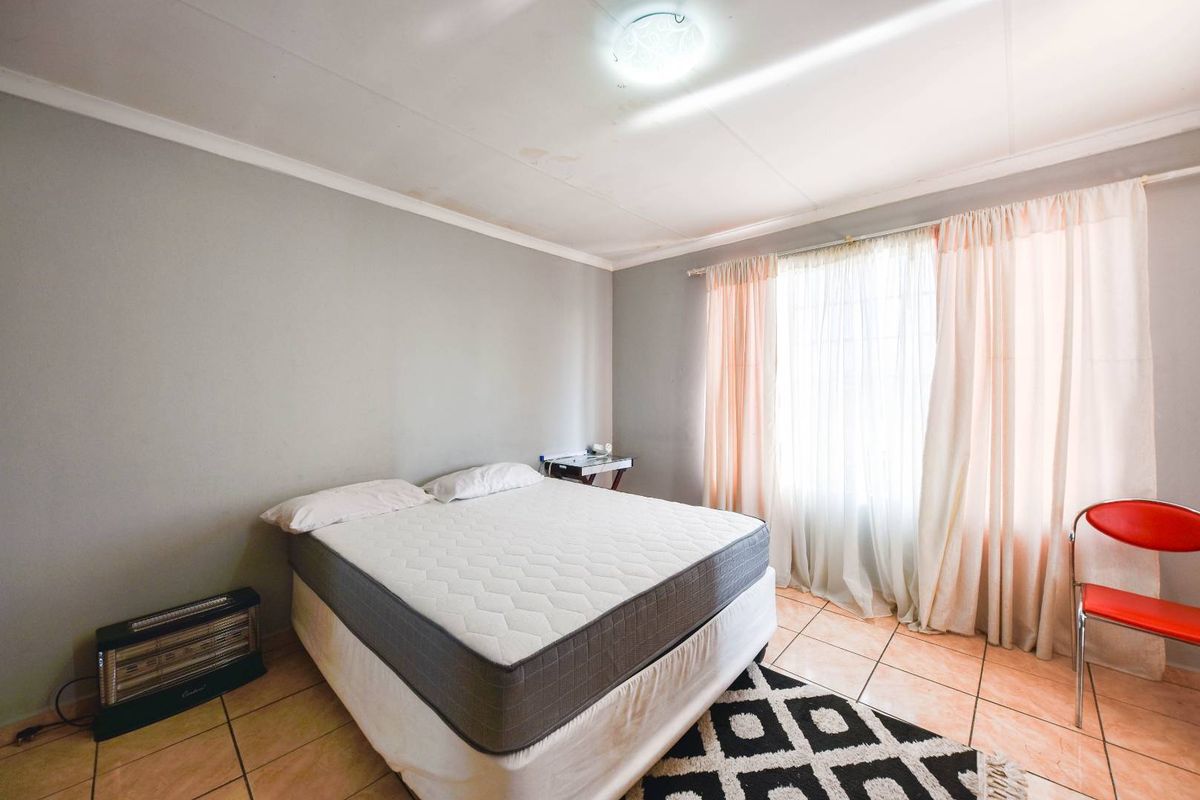A bedroom featuring tiled flooring and natural light through large windows, currently showing signs of ceiling wear and water staining.
