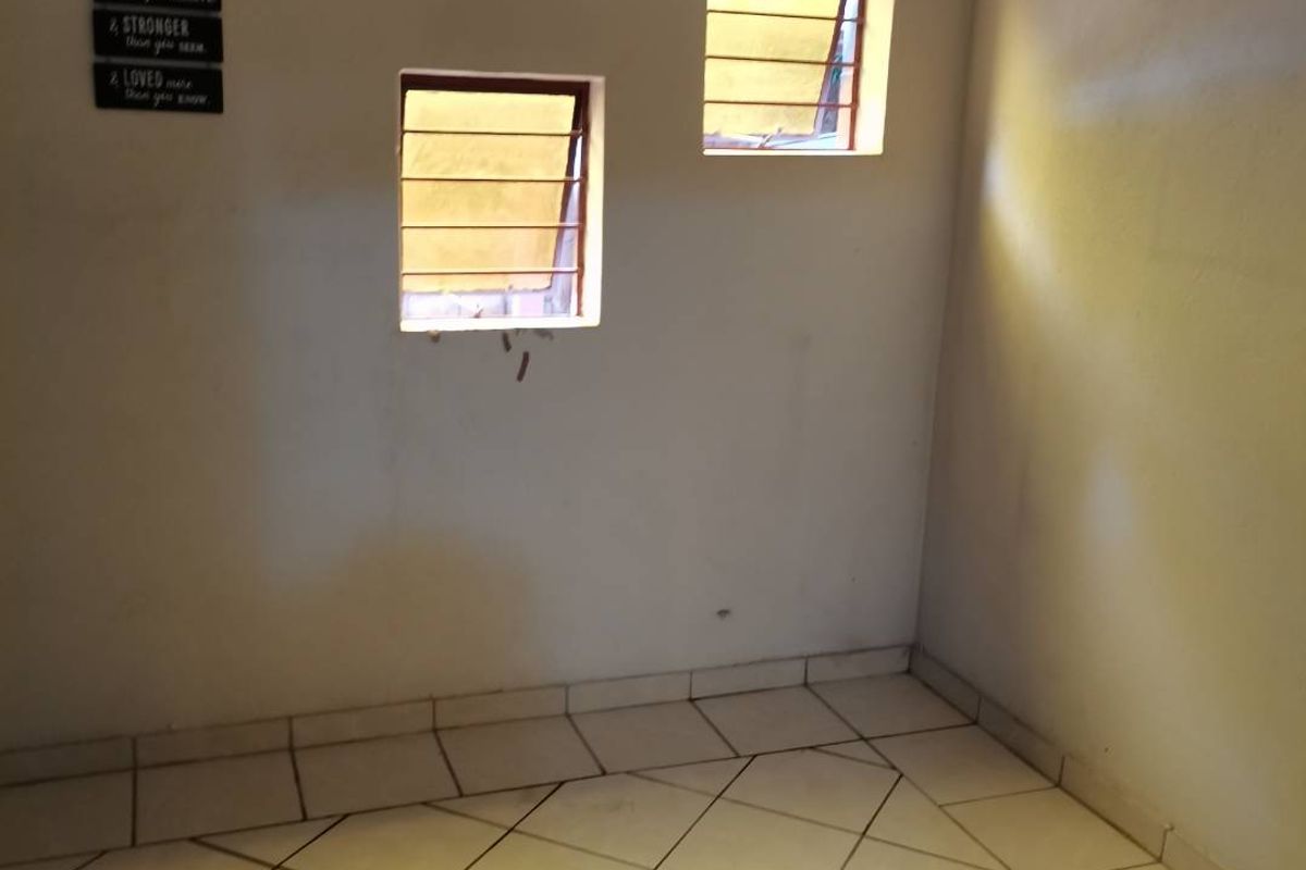 An empty bedroom featuring tiled flooring and two windows with security burglar bars, offering a blank canvas for potential interior updates.