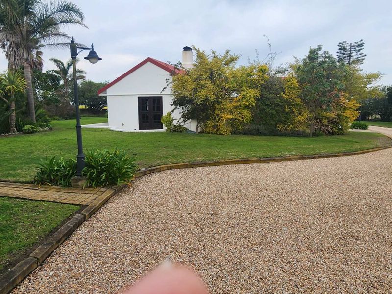 A view of a white farm building with a red roof, surrounded by a well-maintained garden and a gravel driveway.