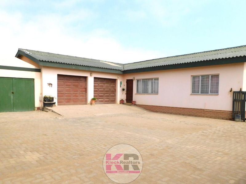Front exterior view of a single-story house featuring a double garage, paved driveway, and secure gated entrance.