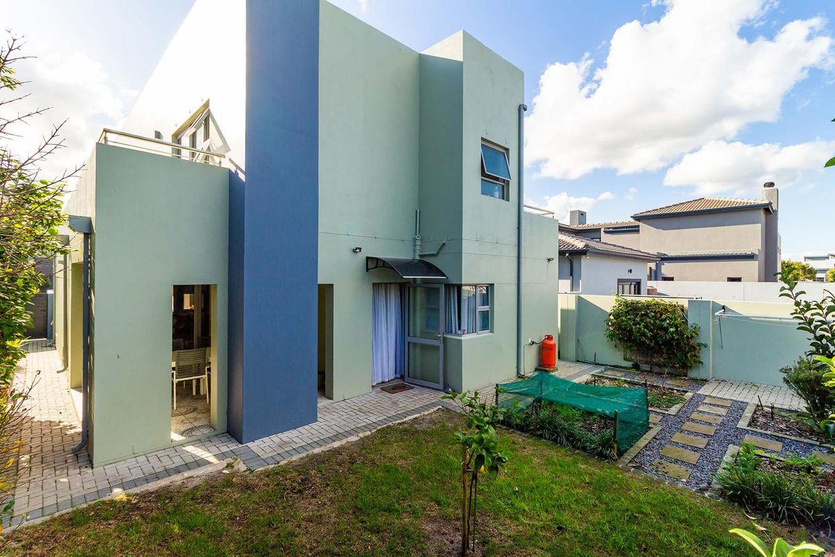 Rear view of the property featuring a paved patio area, small garden, and modern architectural facade with blue and green exterior paint.