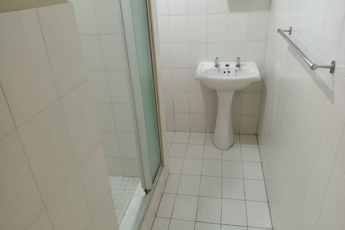 A functional bathroom featuring a pedestal basin, shower enclosure, and fully tiled surfaces, offering a blank canvas for modern renovation.