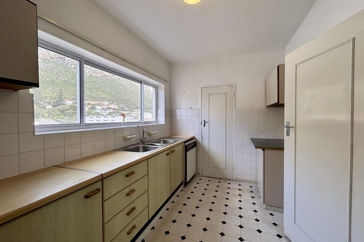 A functional kitchen featuring laminate countertops, built-in cabinetry, a double sink, and tiled flooring with a view of the surrounding landscape.