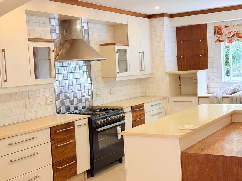 A well-maintained kitchen featuring white and wood-toned cabinetry, stone countertops, a gas stove with an extractor fan, and a central kitchen island.