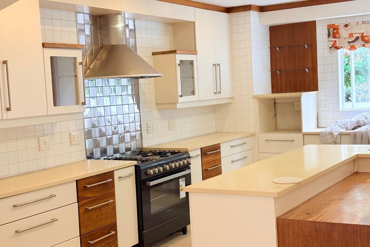 A well-maintained kitchen featuring white and wood-toned cabinetry, stone countertops, a gas stove with an extractor fan, and a central kitchen island.