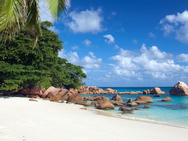 A scenic view of a pristine white sand beach with turquoise waters, large granite boulders, and lush tropical vegetation.