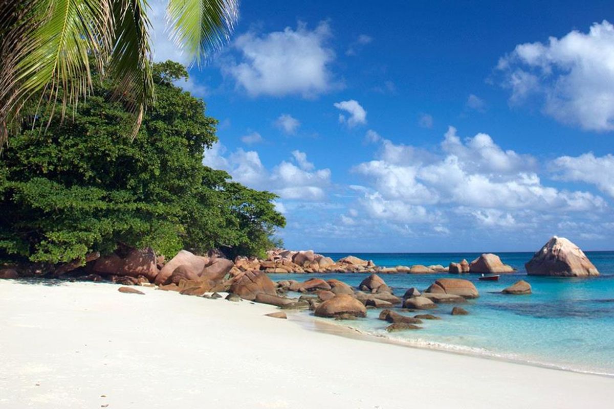 A scenic view of a pristine white sand beach with turquoise waters, large granite boulders, and lush tropical vegetation.
