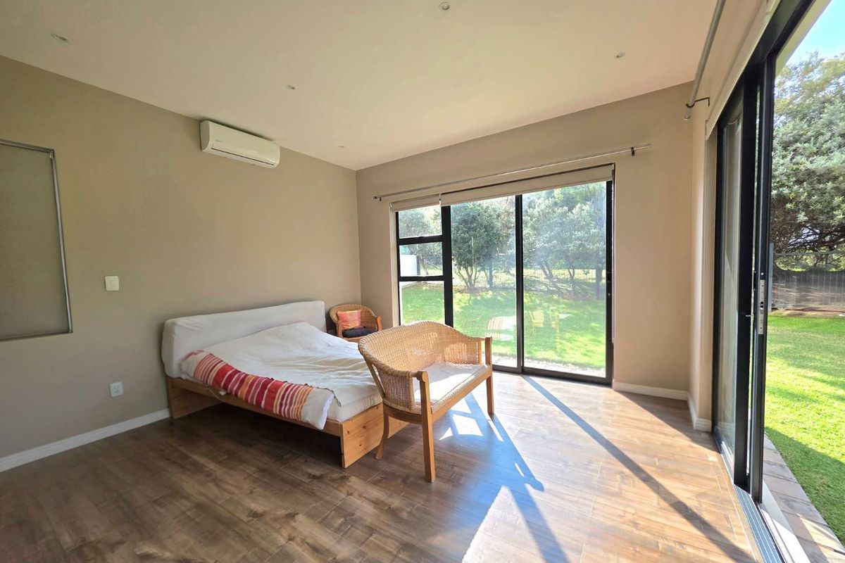 Spacious bedroom featuring wood-look flooring, recessed lighting, a wall-mounted air conditioning unit, and large sliding glass doors providing direct access to the garden.