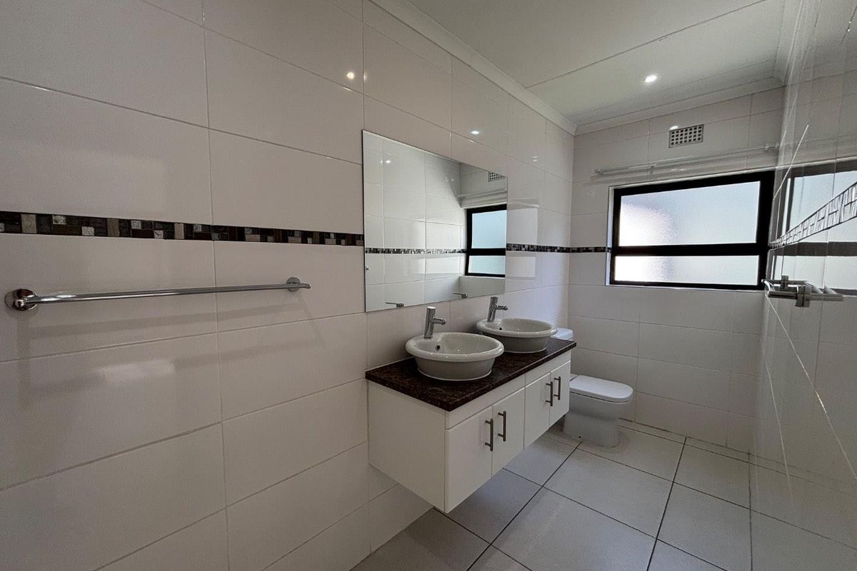 A clean, modern bathroom featuring a double vanity with vessel sinks, granite countertop, wall-mounted cabinetry, and neutral tiled finishes throughout.