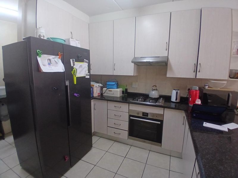 A functional kitchen featuring light-toned cabinetry, dark granite countertops, a gas hob, built-in oven, and tiled flooring.