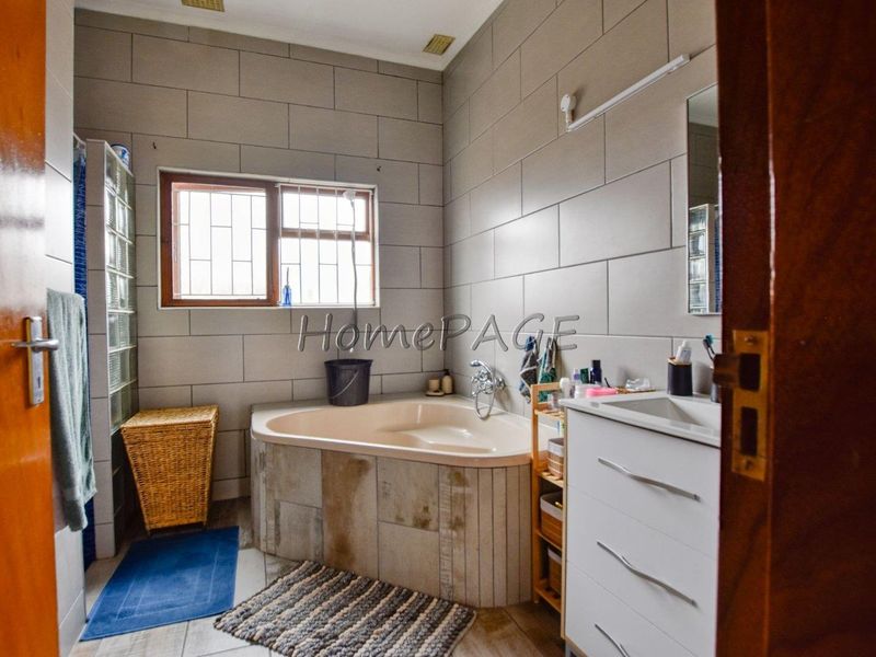 A functional bathroom featuring a corner bathtub, vanity cabinet, and tiled wall finishes, with a window providing natural light.