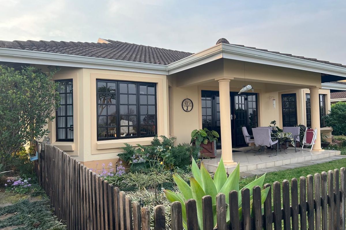 A well-maintained townhouse rear elevation featuring a covered patio, tiled roof, and black-framed windows overlooking a private garden with a timber fence.
