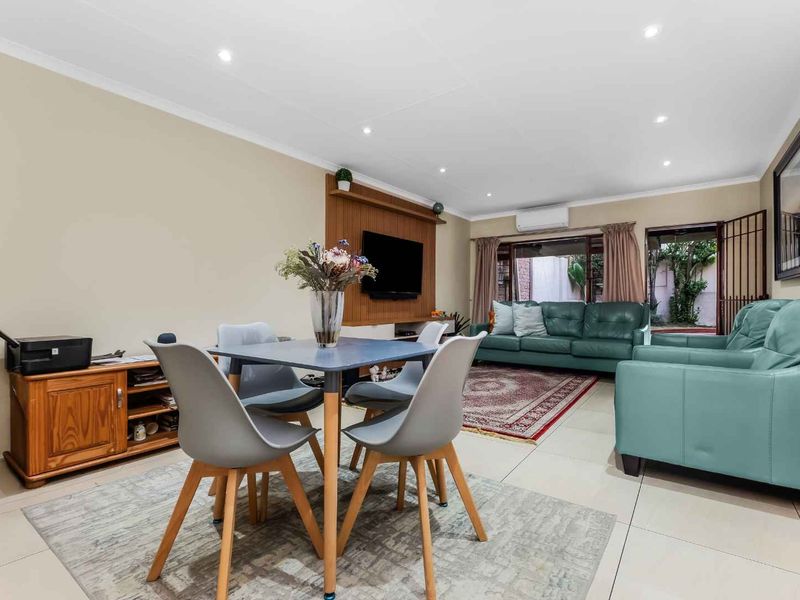 An open-plan living and dining area featuring tiled floors, recessed lighting, a split-system air conditioner, and a timber feature wall.