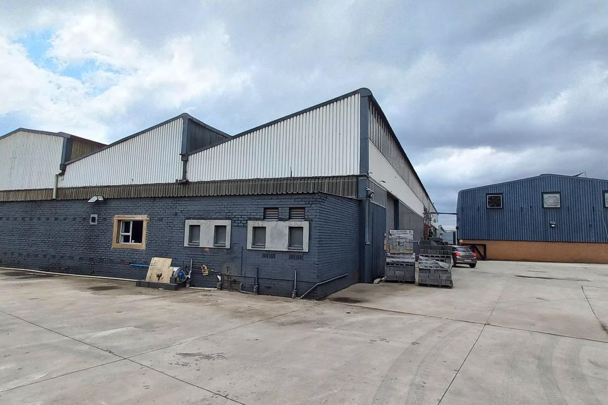 Rear view of an industrial warehouse facility featuring a large concrete yard, corrugated metal roofing, and painted brick exterior walls.