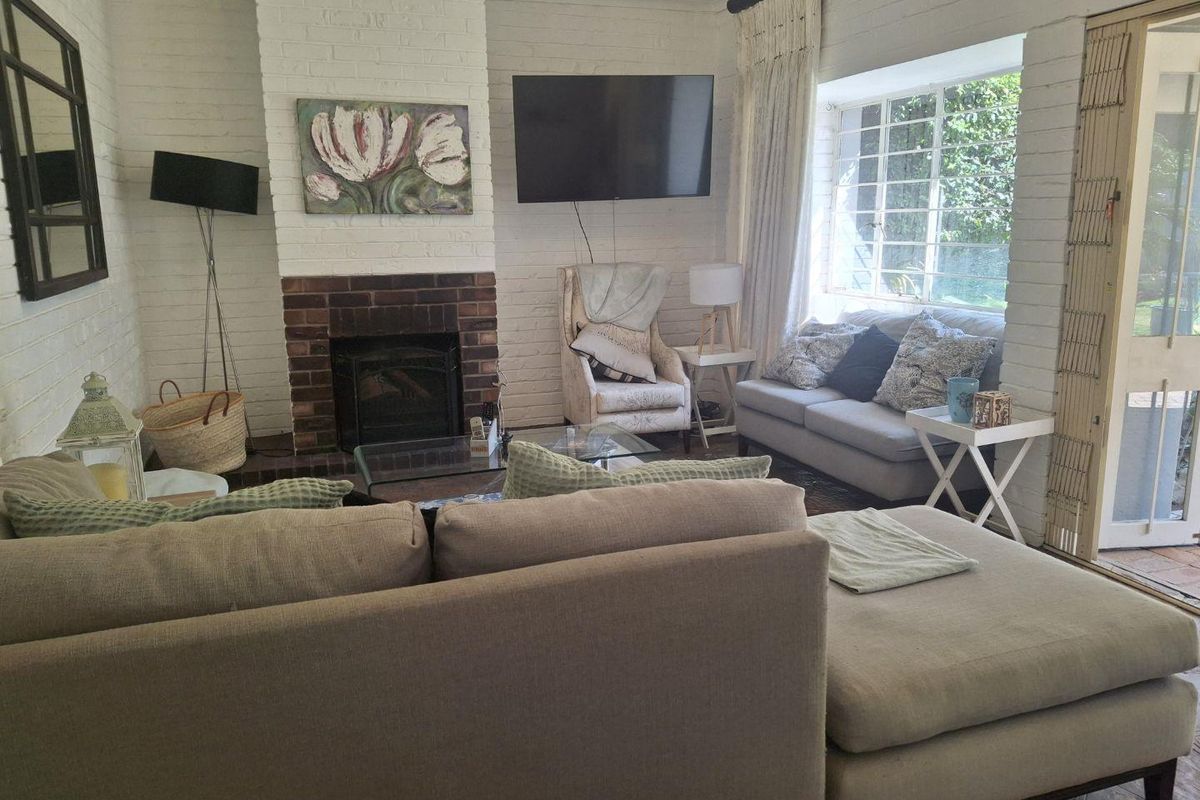 A cozy living room featuring a painted brick fireplace, large steel-framed windows, and direct access to the outdoor area.