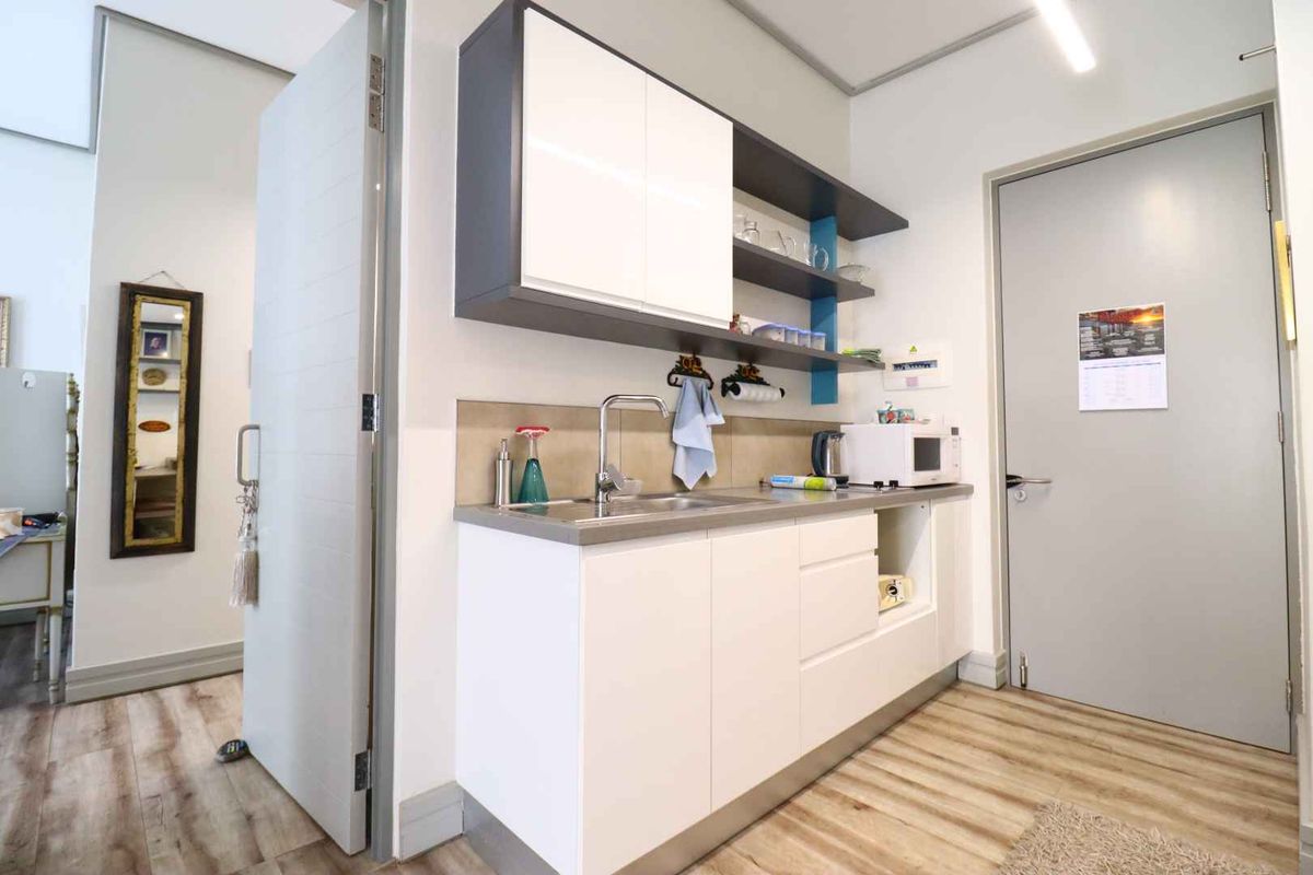 A compact kitchenette featuring modern white and grey cabinetry, a stainless steel sink, tiled splashback, and durable laminate flooring.