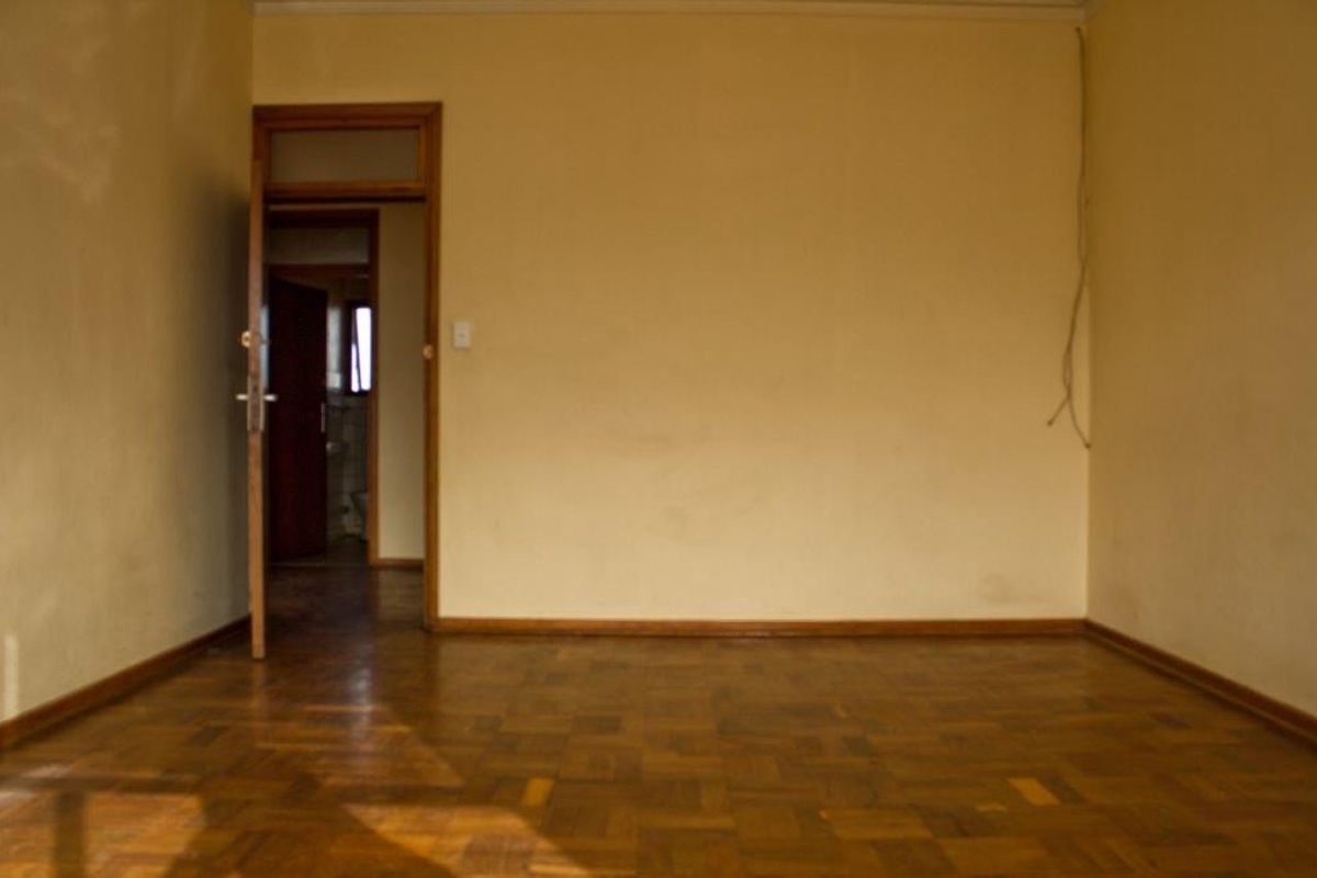 An empty living room featuring original parquet flooring and wooden door frames, requiring cosmetic updates to the walls and electrical fixtures.