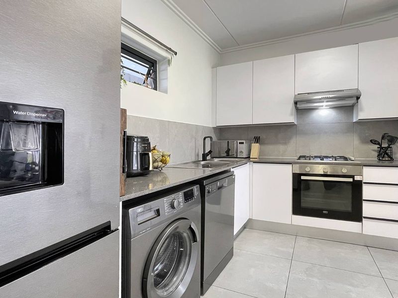 Modern kitchen featuring white cabinetry, stone countertops, gas hob, built-in oven, extractor fan, and tiled finishes with integrated appliance spaces.