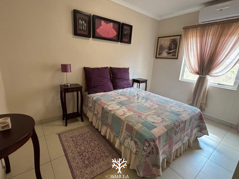 A functional bedroom featuring tiled flooring, a wall-mounted split-system air conditioner, and security burglar bars on the window.
