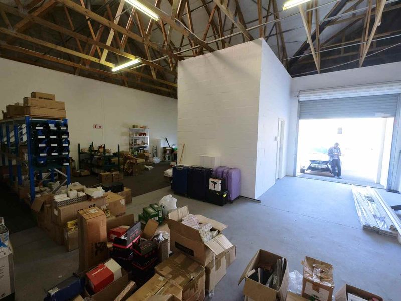 Industrial utility space featuring exposed timber roof trusses, concrete flooring, and a large roller shutter door for easy access.